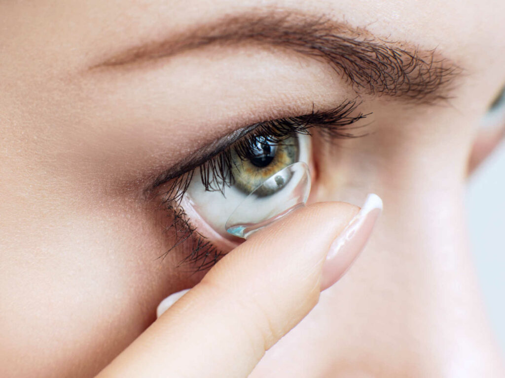 Close up image of a woman putting a contact into her right eye.