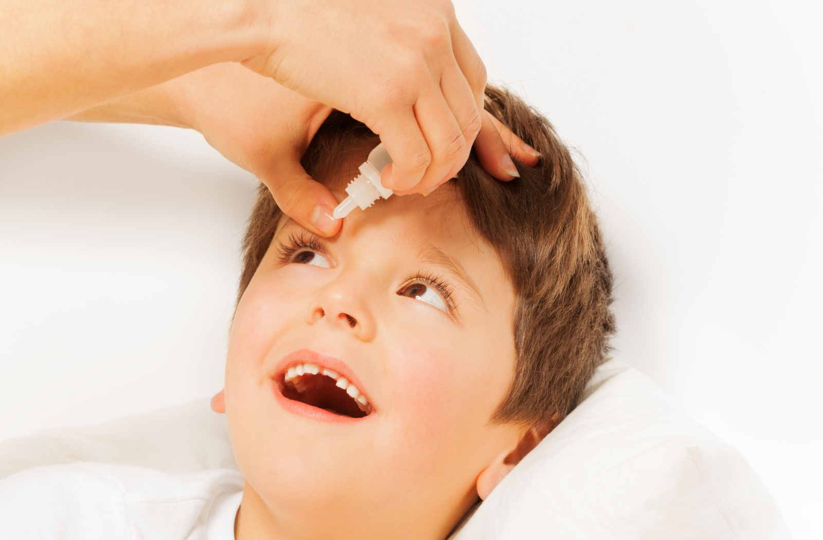 A woman puts atropine eye drops into the right eye of a young happy boy.