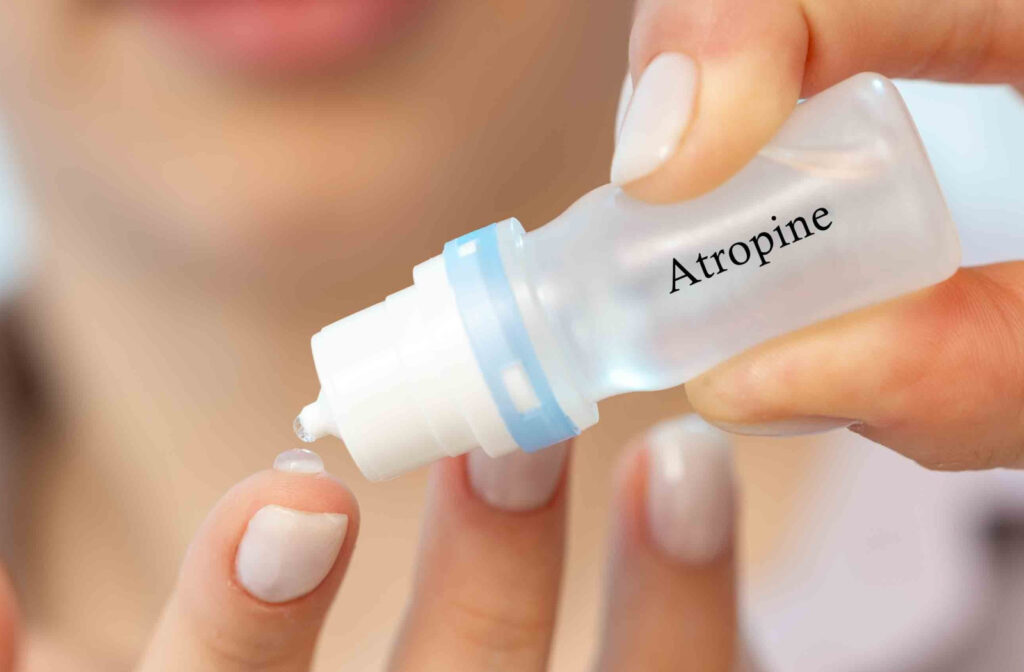 A woman holding a bottle of atropine putting a drop on her finger.